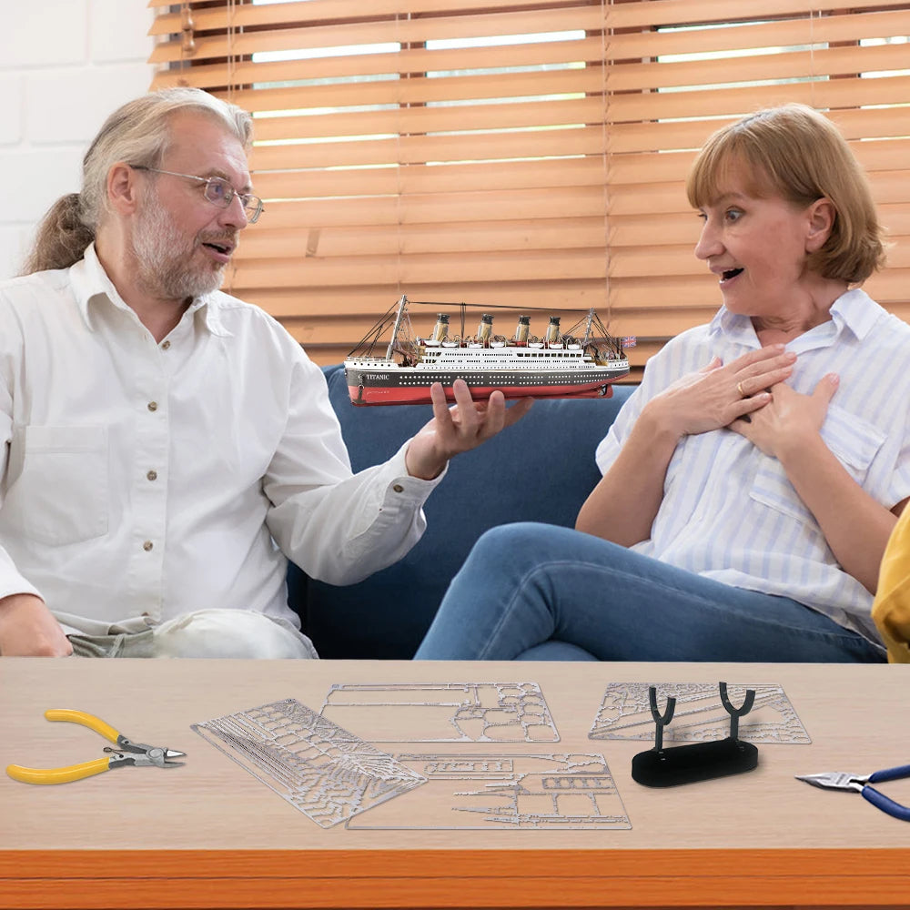 Two people sitting on a couch with a model ship in the background, surrounded by model-making tools and materials.
