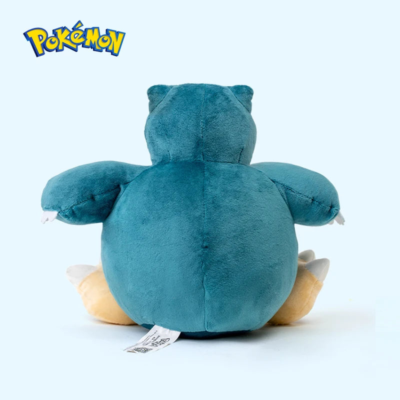 Snorlax plush toy rear view with a blue and beige color scheme on a light gray background, featuring the Pokémon logo.