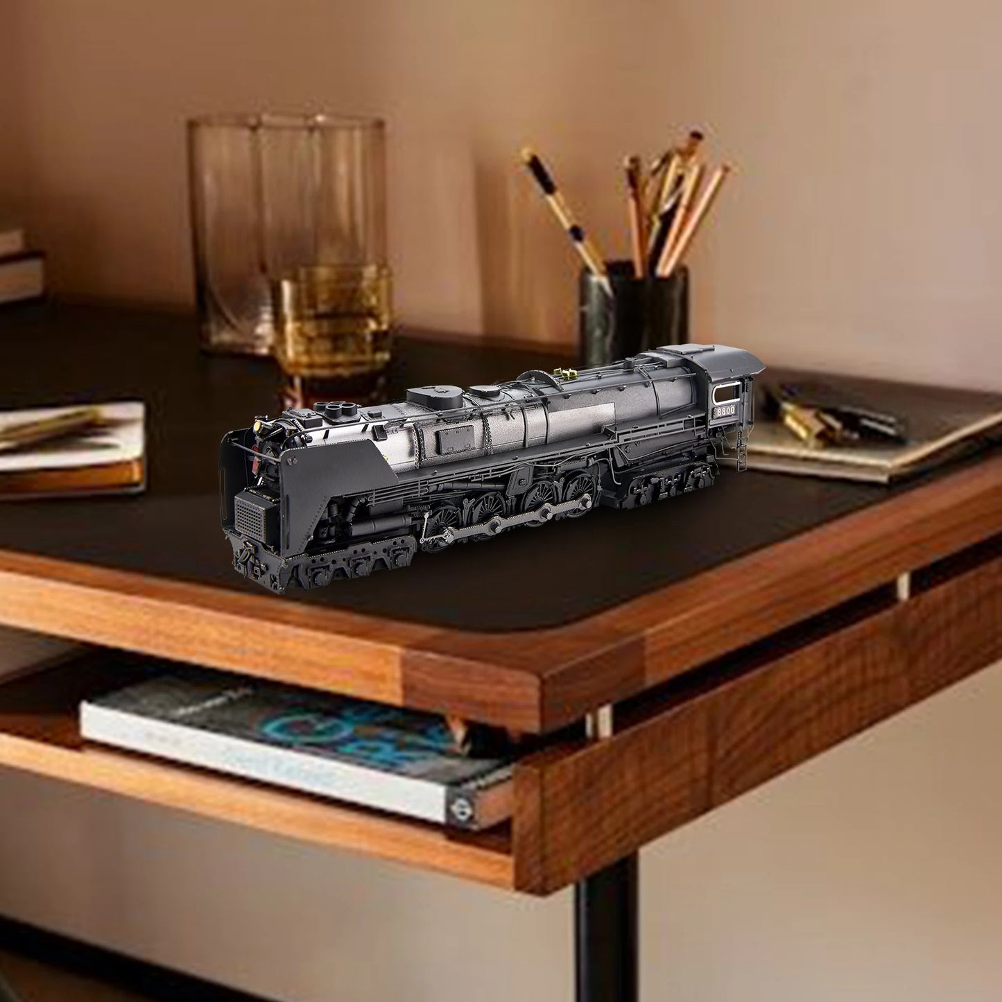 Model train on a desk with books and a glass in the background