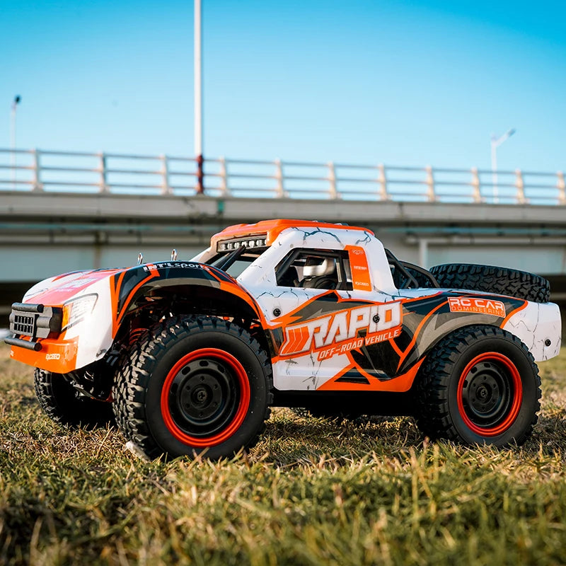 Orange and white remote control car on grass with a bridge in the background