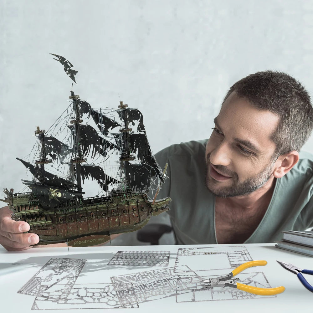 Man holding a model ship with blueprints and tools on a table