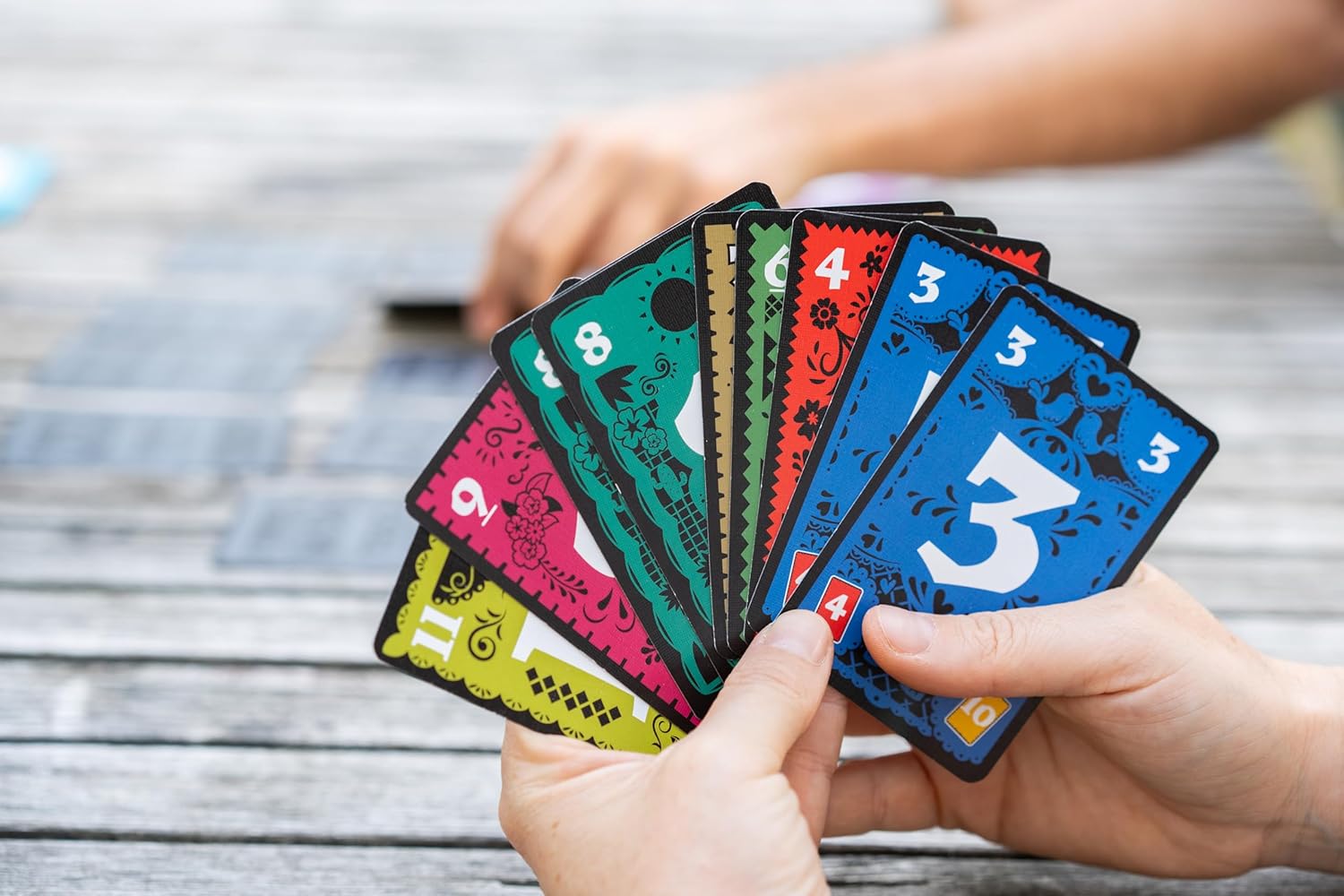 Hands holding colorful playing cards on a wooden surface