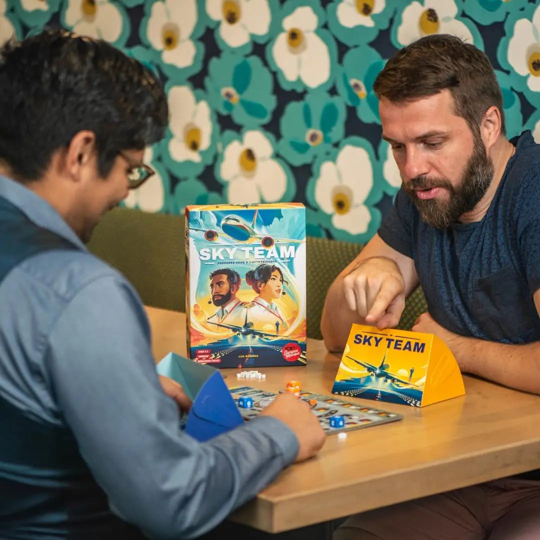 Two men playing a board game with 'Sky Team' branding against a floral wall.