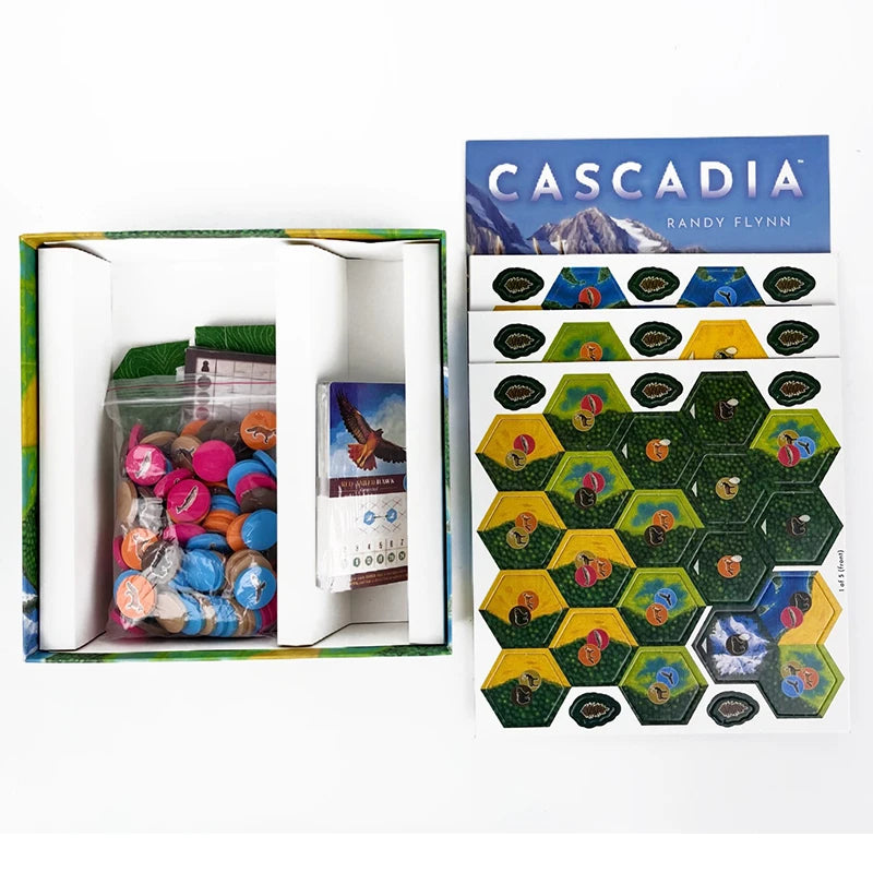 Board game components including hexagonal tiles and a box with 'Cascadia' branding.