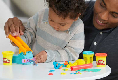 Child playing with Play-Doh toys at a table with an adult next to them.