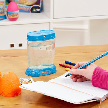 The Original Sea Monkeys - Ocean Zoo Grow Your Own Pets Science Kit 6+ years Child's hand holding a pen over a notebook with a blue container and toys in the background