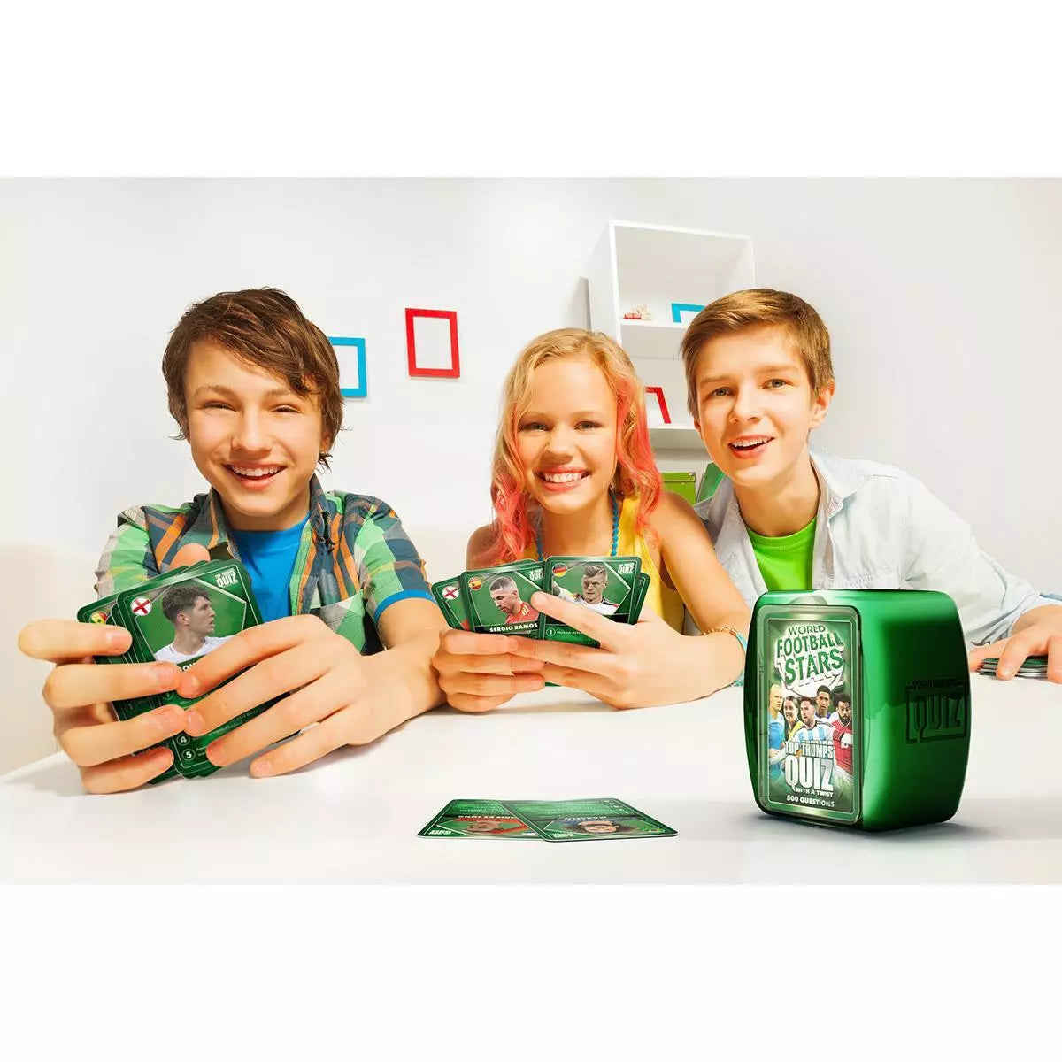 Three children playing with a 'Football Stars Quiz' card game on a white table.